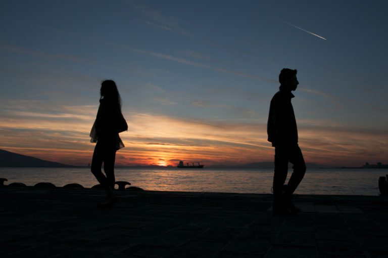 A man and woman standing on the beach at sunset.