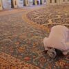 A person kneeling down on the floor in front of an ornate rug.