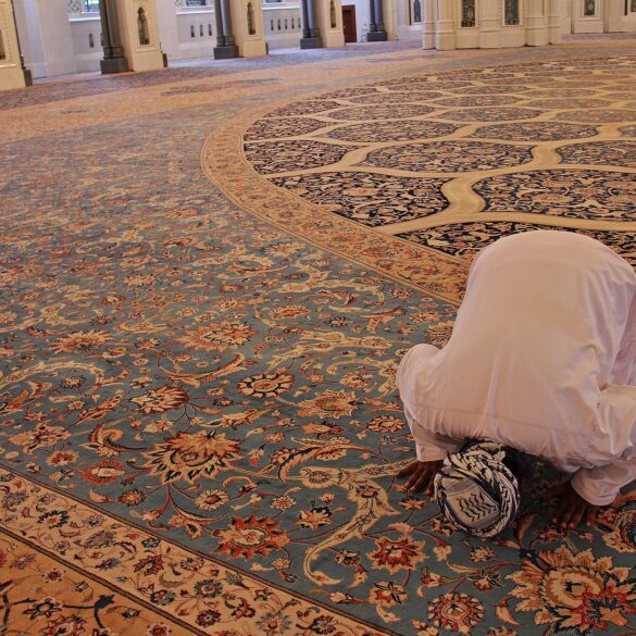 A person kneeling down on the floor in front of an ornate rug.
