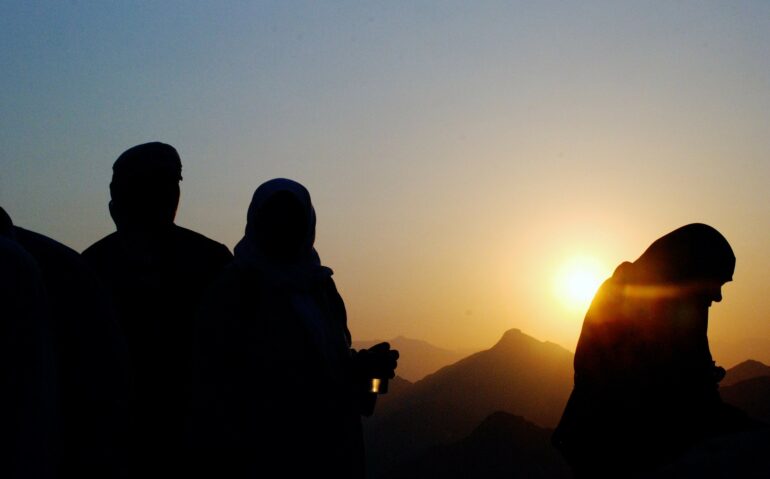 A couple of people standing in front of the sun.
