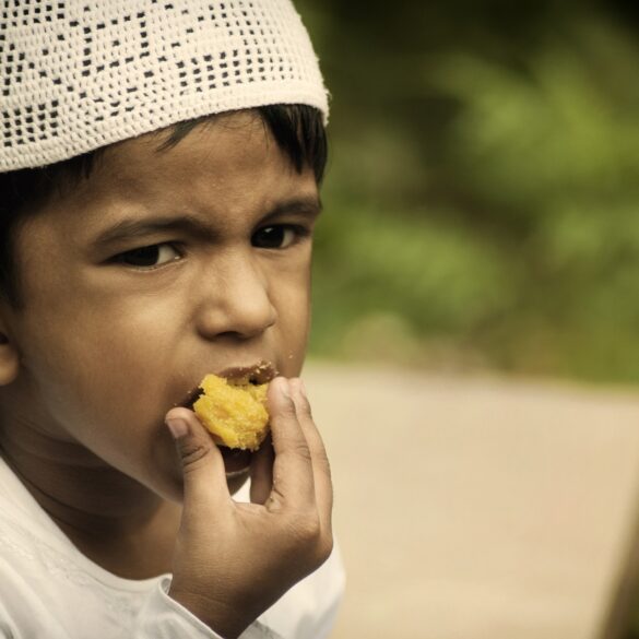 A boy in white shirt eating food near trees.