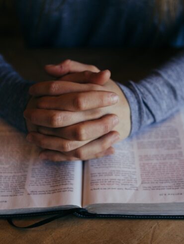 A person is praying on top of an open bible.