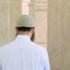 A man with a beard and hat is standing in front of a wall.