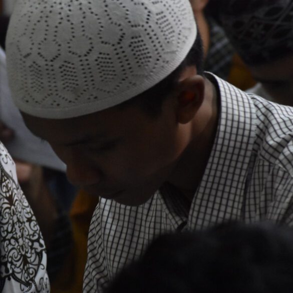 A man in white hat and black shirt standing next to other people.