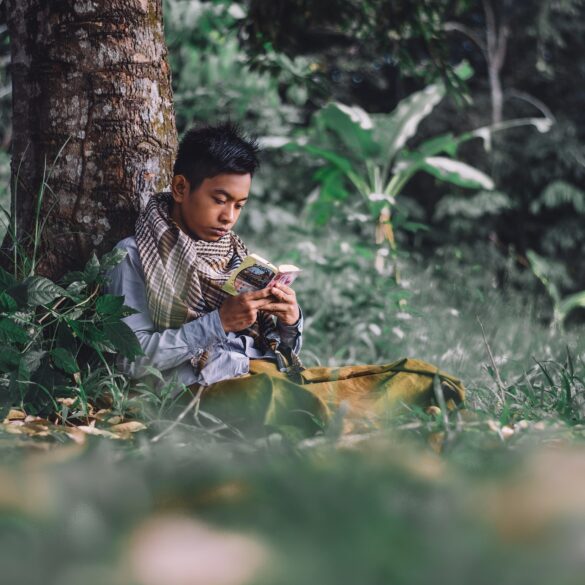 A boy sitting in the grass with a camera.