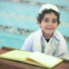 A young boy sitting at a table with an open book.