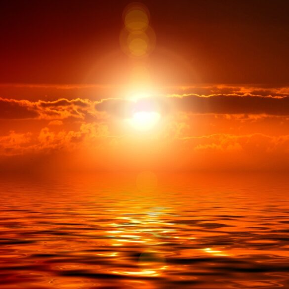 A bright sun setting over the ocean with clouds.