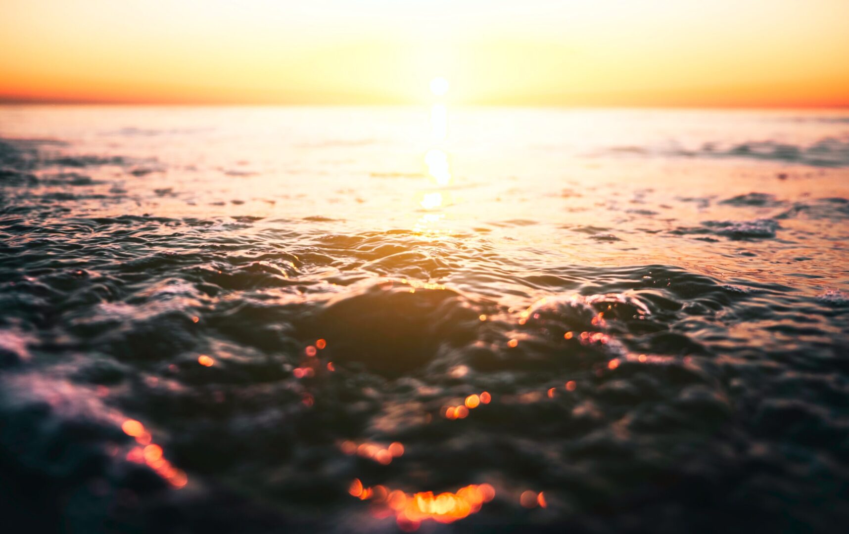 A sunset over the ocean with water in front of it.